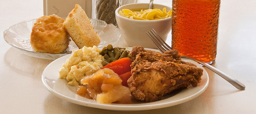 dinner plate of fried chicken, vegetables, cornbread and dessert
